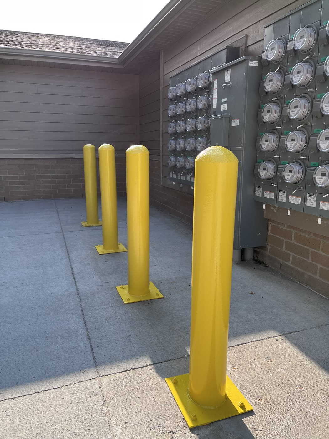 Yellow painted posts on a concrete pad beside a wall of utility meters