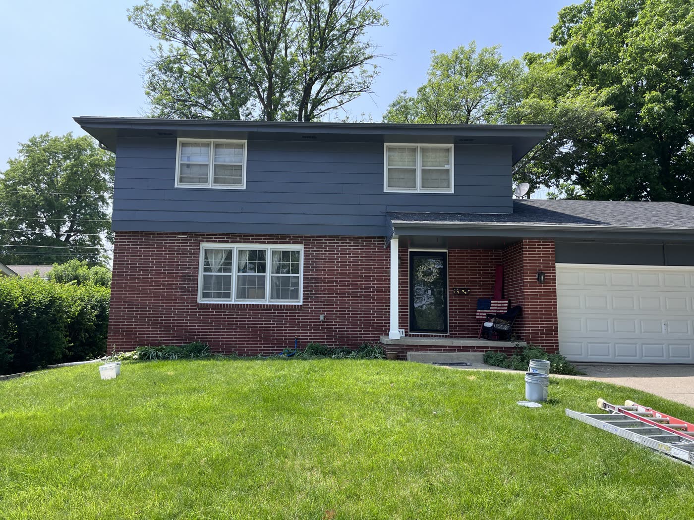 Front of a house with blue-gray siding, brick base and white garage door